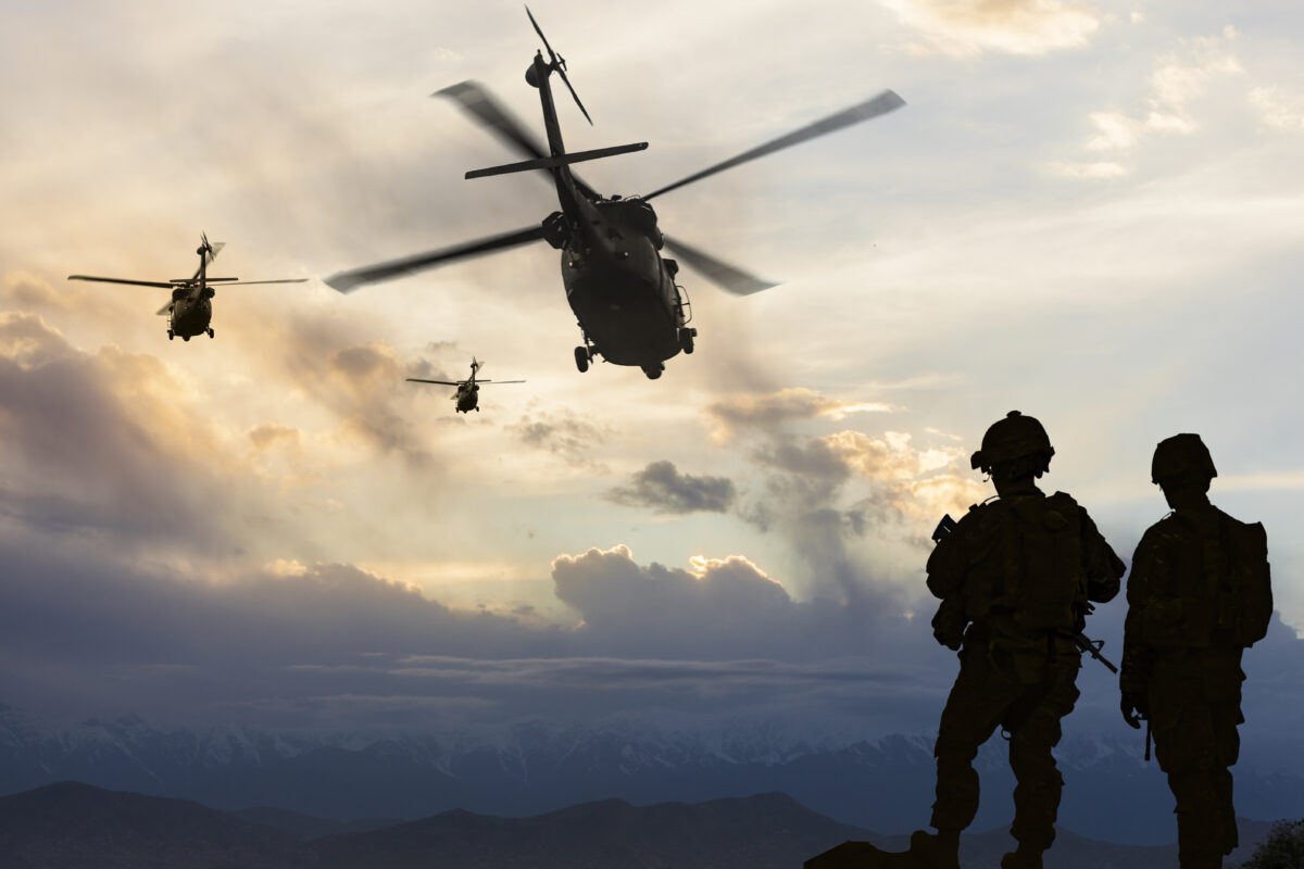 Military helicopters leave behind soldiers for a mission at dusk.